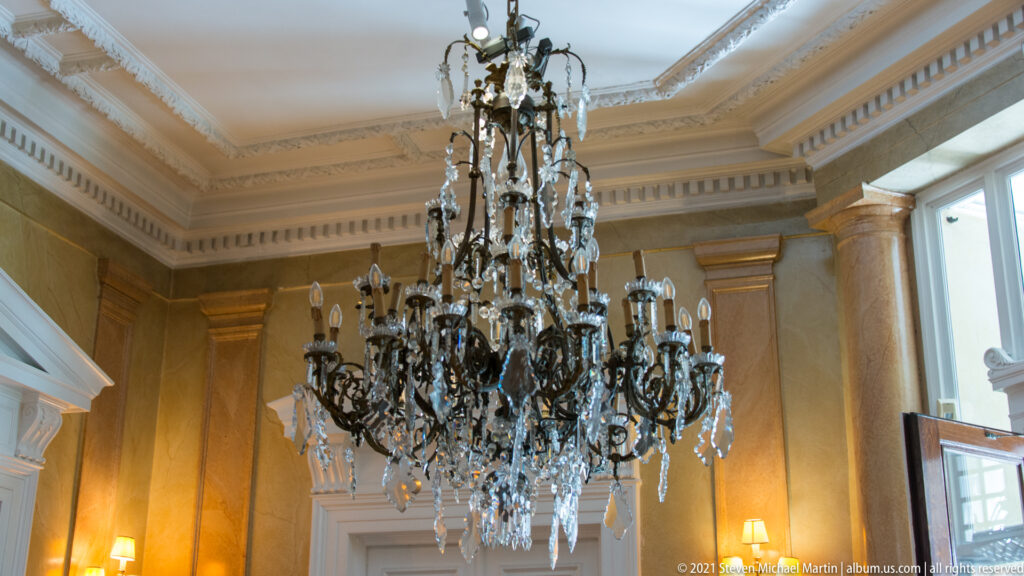 Large ornate chandelier with crystal drops hanging beneath a molded ceiling.