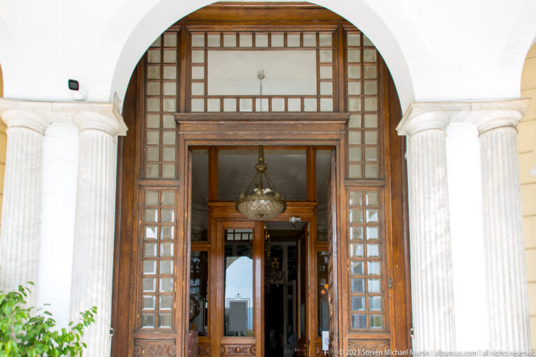 Tall wooden and glass museum entrance framed by fluted columns and a white arch.