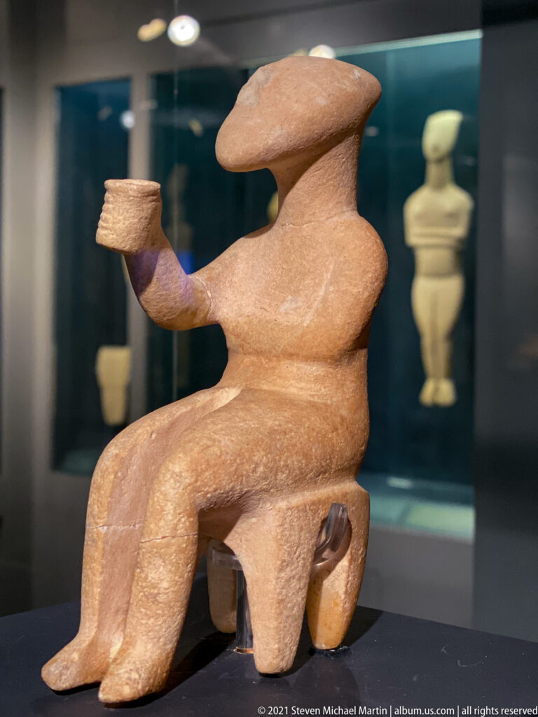 Cycladic marble Cup-bearer seated on a stool and extending a small cup in his right hand.