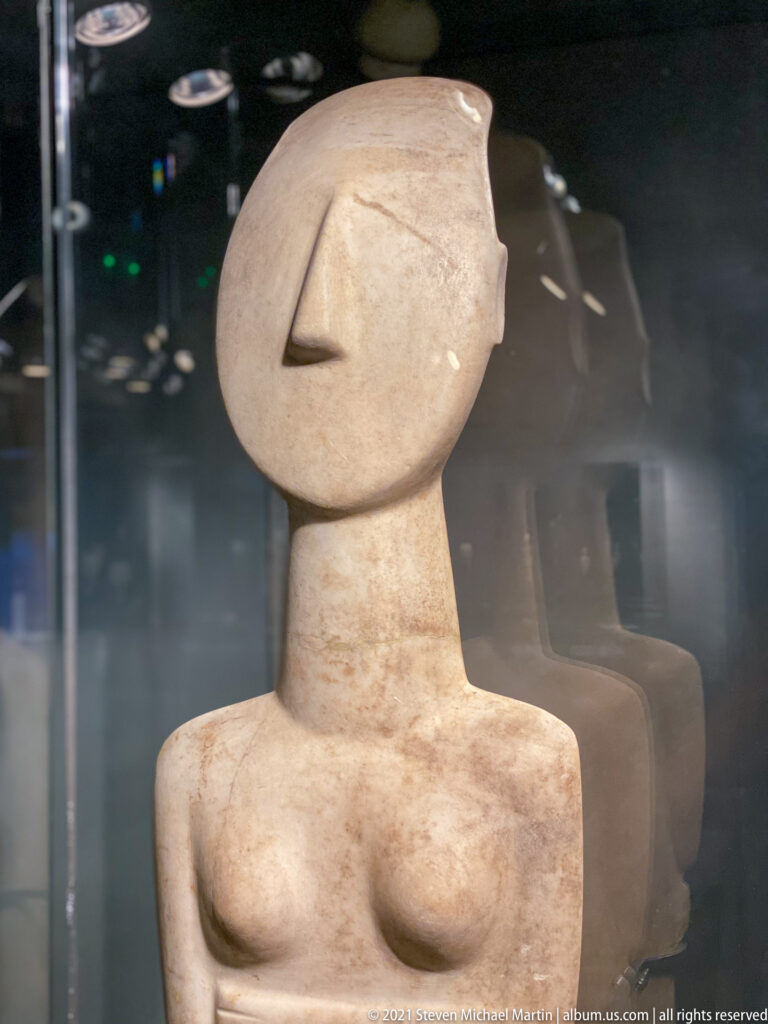 Upper body of pale Cycladic marble female figure with long nose and simplified face.