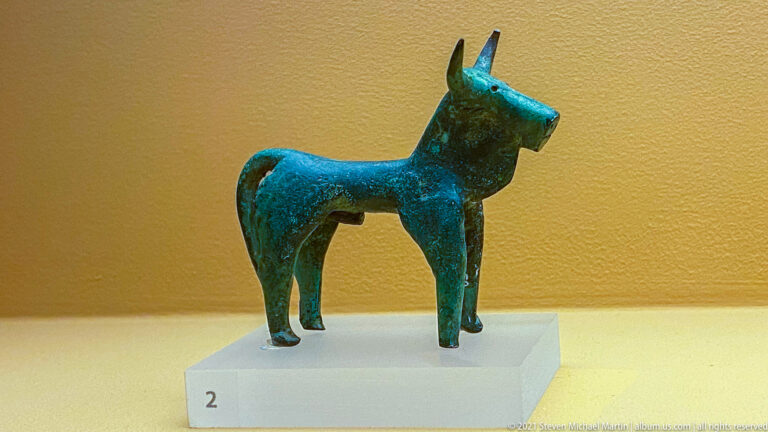 Small Geometric-period bronze horse with elongated neck, cylindrical body, slender legs, pointed ears, and green patina.