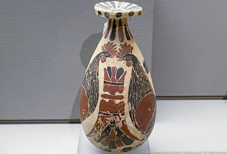 Small painted ceramic bottle with narrow neck, flaring rim, bird-like motif, and geometric decoration on a pale body.