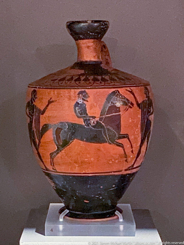 Low, lidded black-figure ceramic vessel with a running horse on the orange body and dark painted bands.