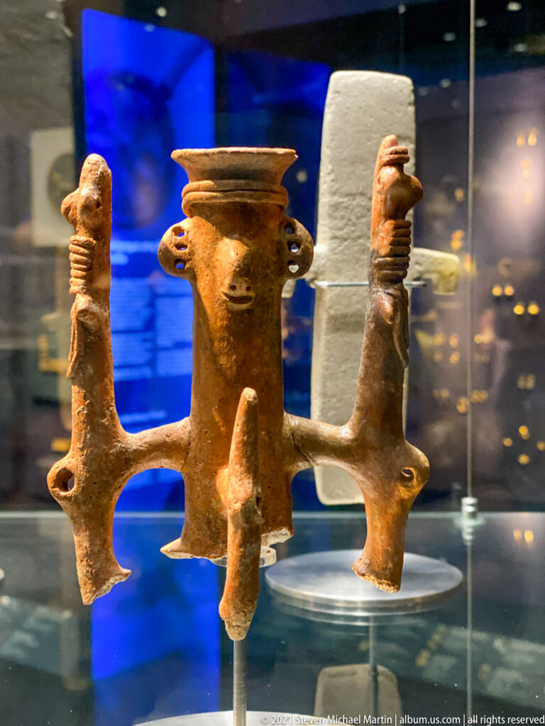 Terracotta composite vessel with a central cup and multiple projecting modeled figures or supports, displayed in a glass case.