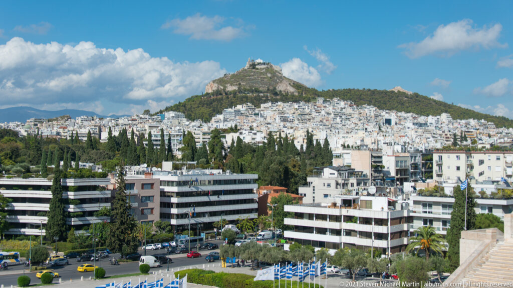 Mount Lycabettus rising above dense white apartment buildings and trees in central Athens.