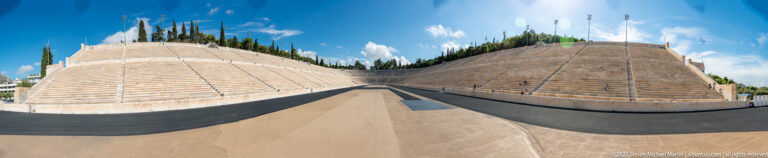 Track-level wide-angle view down the Panathenaic Stadium between steep, symmetrical marble seating banks.