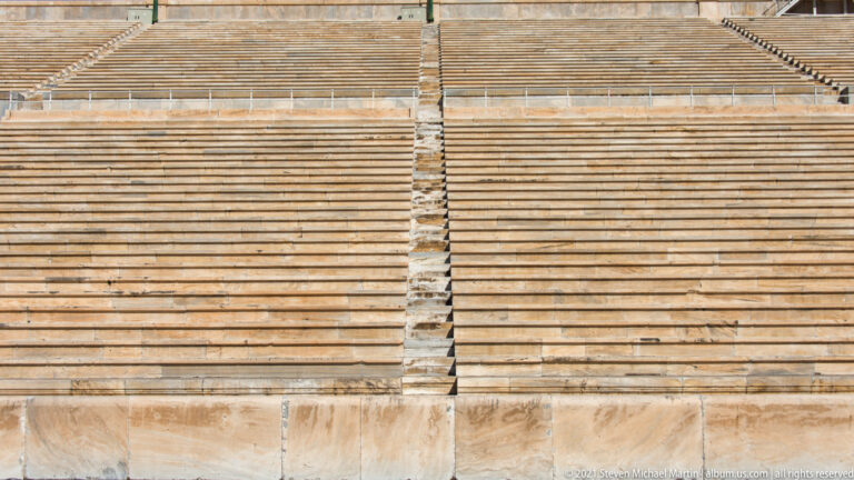 Frontal detail of marble stadium benches divided by a narrow vertical stair aisle.