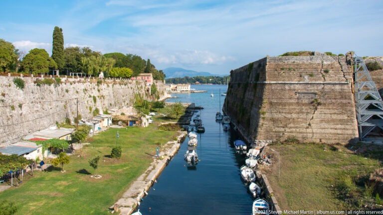 Wide view of the Contrafossa beside a massive Old Fortress bastion, with moored boats and stone walls.