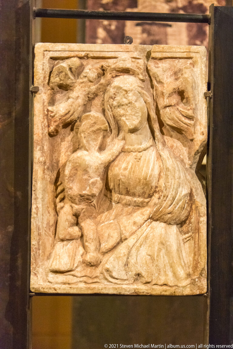 Weathered rectangular stone relief with a reclining or seated human figure and heavily eroded surrounding forms.