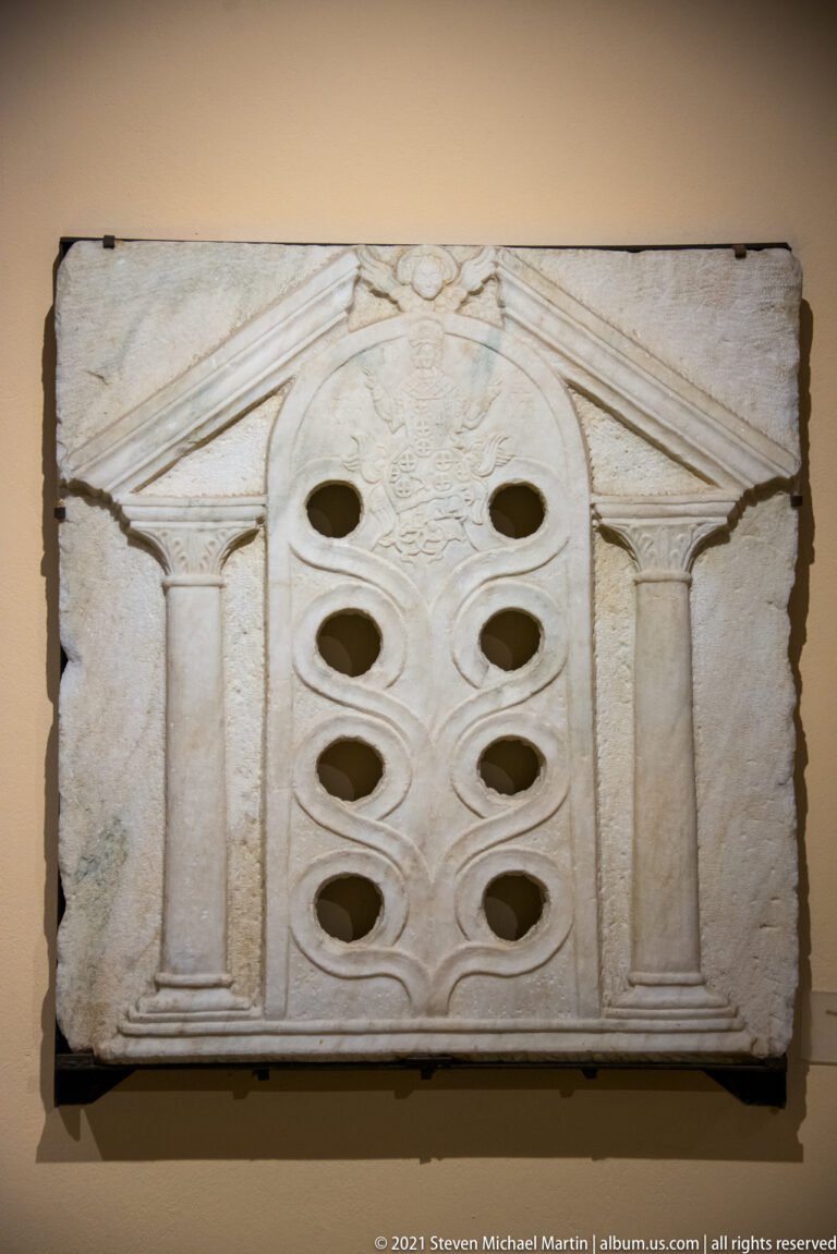 Rectangular carved stone slab with miniature pediment and columns surrounding eight oval perforations.
