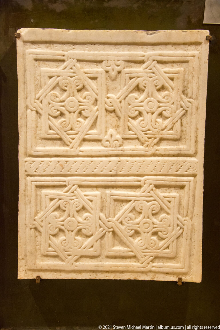 Rectangular pale stone slab with two registers of interlaced braided ornament and central cross motifs.