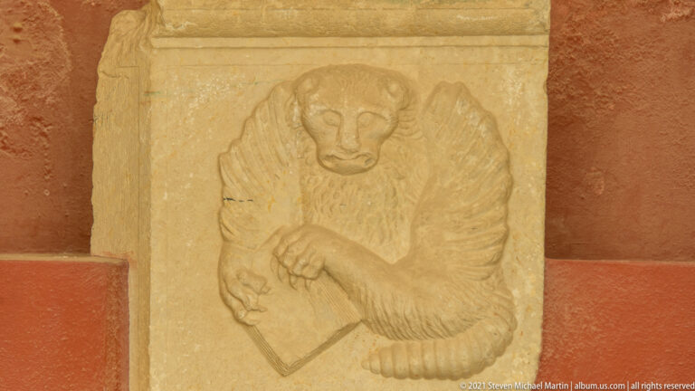 Weathered stone relief of a seated ape-like figure with bent limbs and a rectangular object.