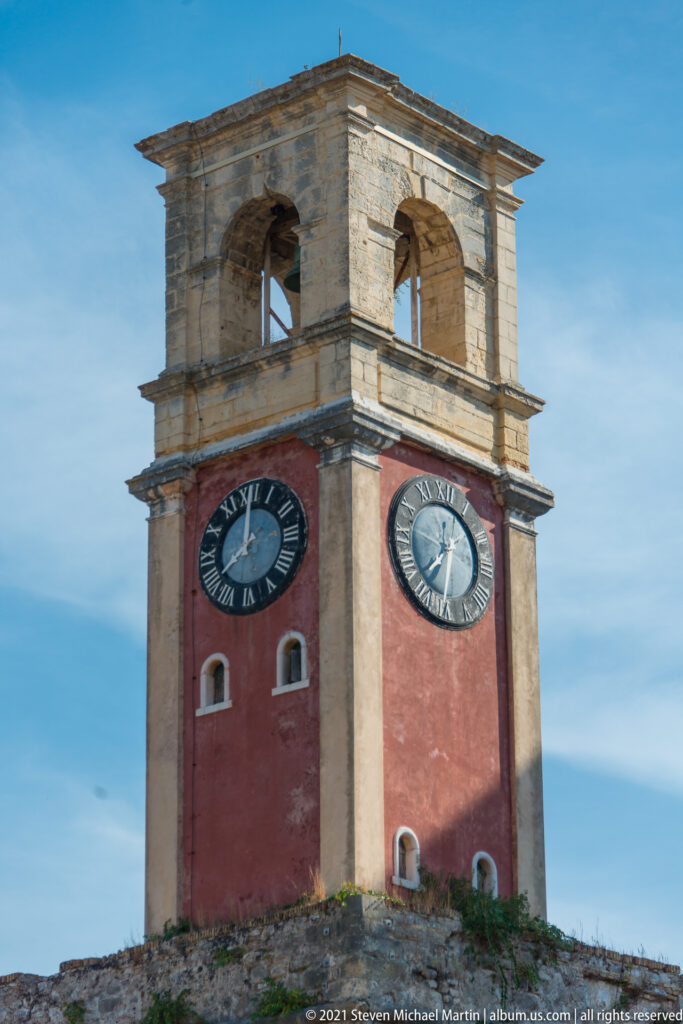 British-era Old Fortress clock tower with red lower shaft, clock faces, and Maltese-stone belfry.