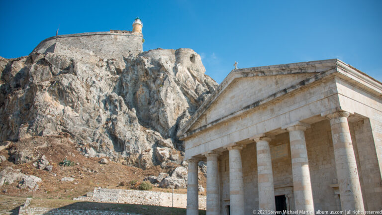 Doric portico of the Church of Saint George below the rocky Old Fortress summit and lighthouse.