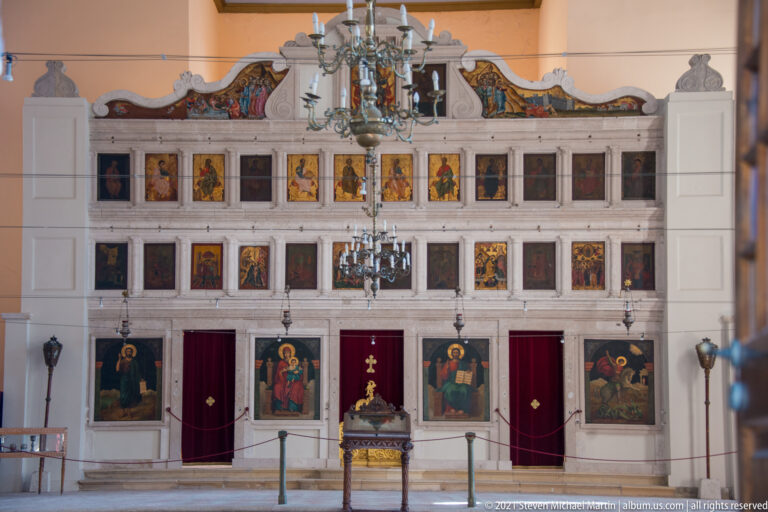 Stone iconostasis in the Church of Saint George with tiered icons, red-curtained doors, chandeliers, and liturgical furnishings.
