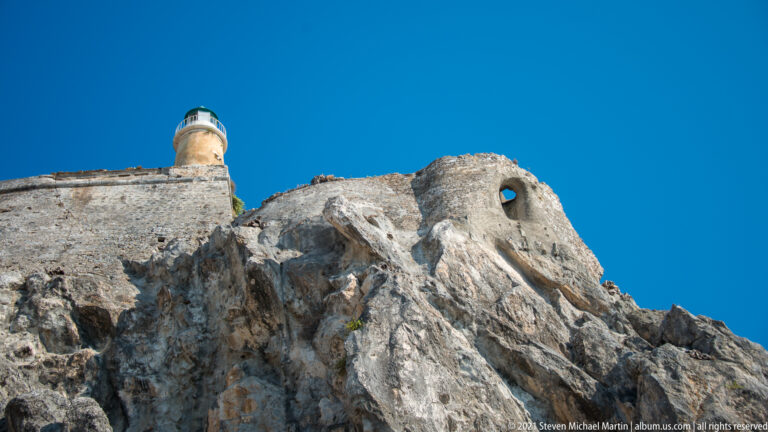Old Fortress lighthouse above steep pale rock and masonry walls, with a small arched opening cut into the defense.