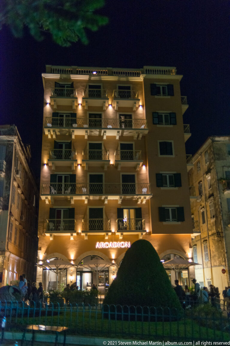 Arcadion Hotel façade at night with stacked balconies, warm exterior lights, café seating, and illuminated ARCADION sign.