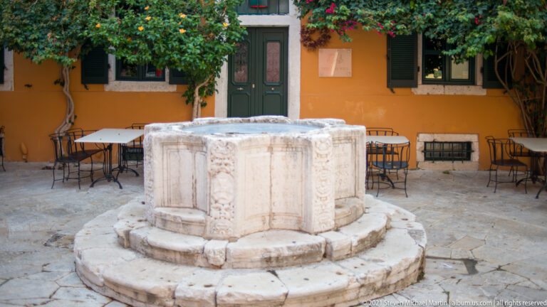 Carved 1699 cistern wellhead in Kremasti Square with relief masks, coats of arms, floral ornament, and inscriptions.