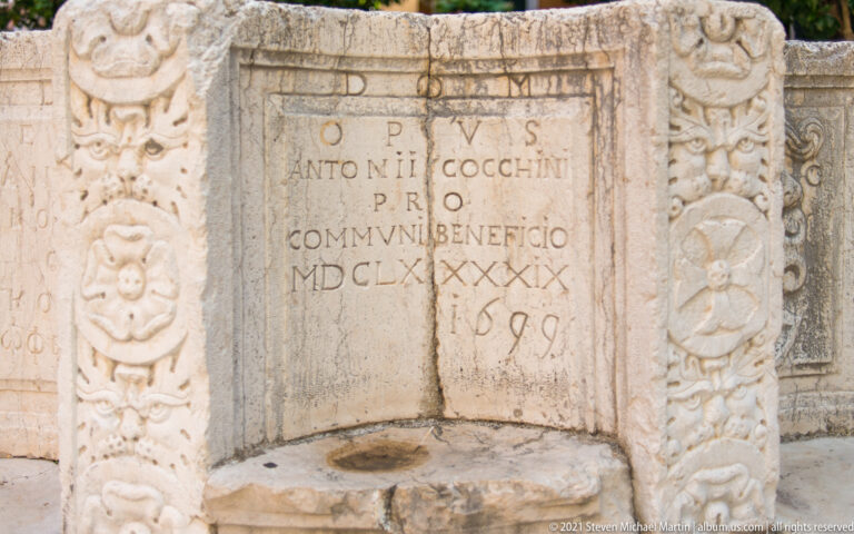 Inscribed panel dated 1699 on the Kremasti Square cistern wellhead, bordered by floral and mask relief carving.