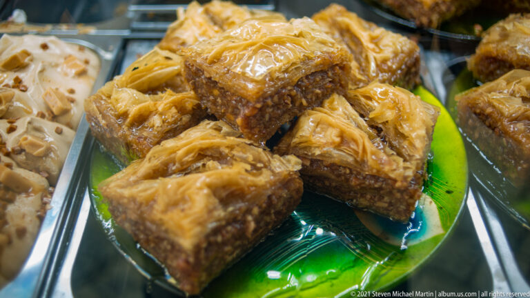 Close view of square layered phyllo pastries filled with chopped nuts and glazed with syrup on a green plate.