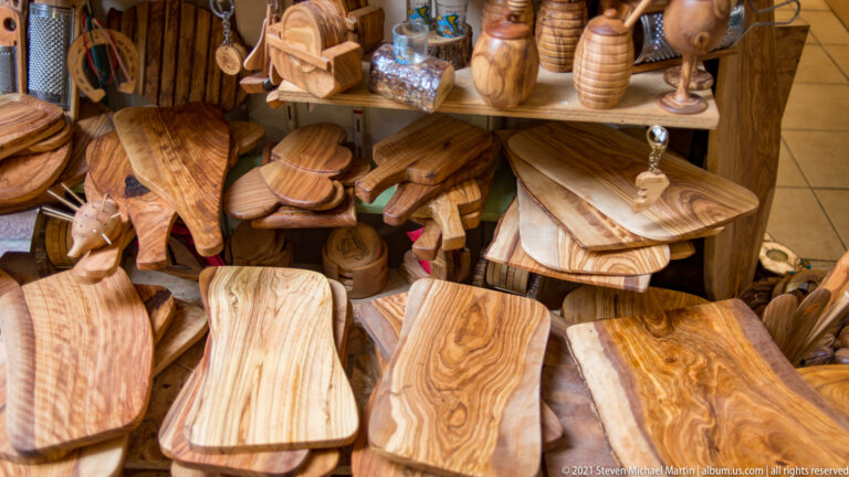 Shop display of polished olive-wood cutting boards, trays, bowls, vessels, and small carved objects with prominent grain.
