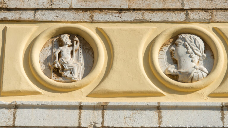 Two circular stone relief medallions in a yellow band, one with a small classical figure scene and one with a profile bust.