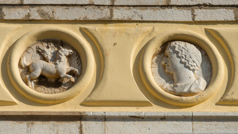 Two circular stone reliefs set in a yellow wall, one with a figural scene and one with a profile head.