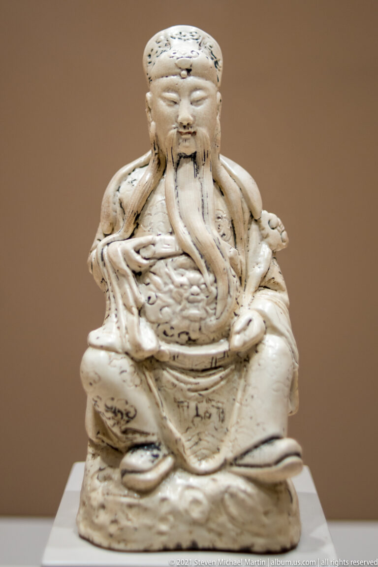 White-glazed Ming porcelain figure of Guandi seated in elaborate robes, with official headgear, long moustache, and flowing beard.