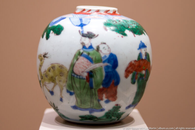Rounded white porcelain jar painted in green, red, blue, and yellow with several Chinese figures among rocks and foliage.