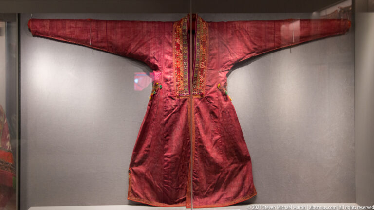 Long red robe with outstretched sleeves and dense multicolored embroidery along the neck and front opening.