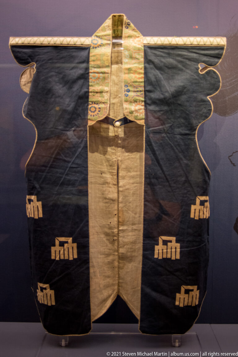 Dark Japanese robe with broad sleeves, pale central panels, patterned collar, and repeated light motifs near the lower sides.