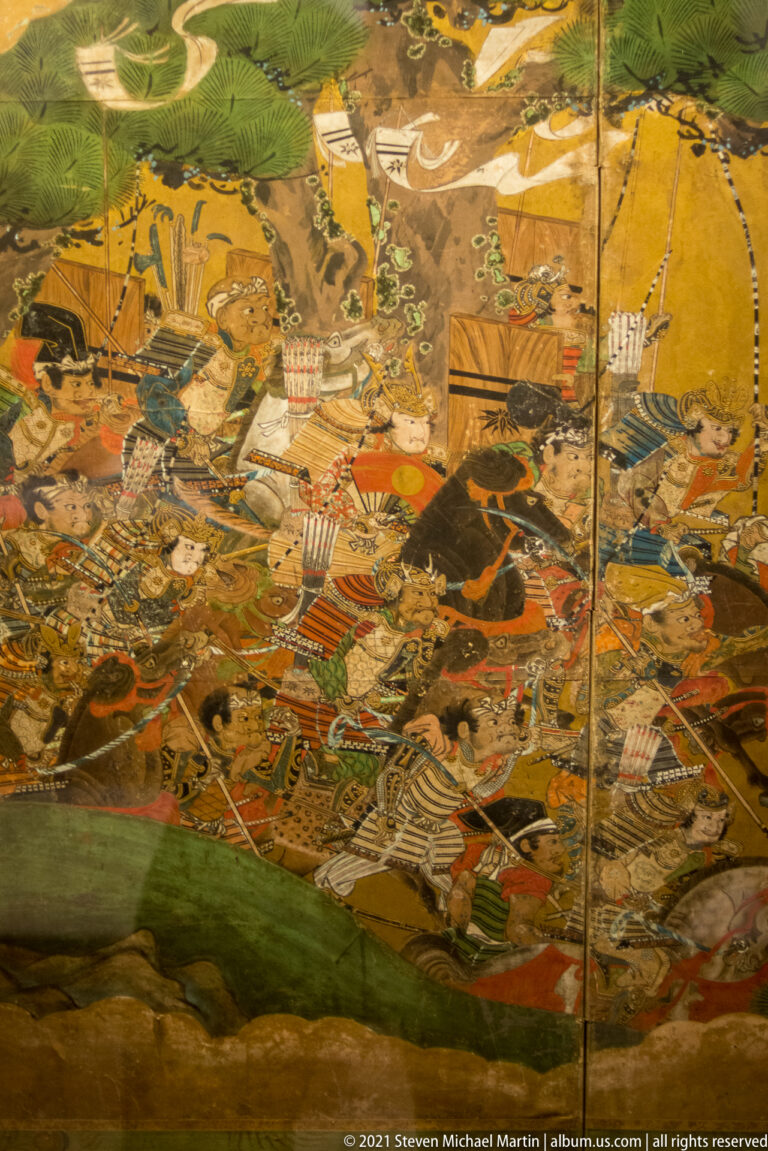 Gold-ground Japanese folding screen detail crowded with armored warriors, horses, banners, and weapons in battle.