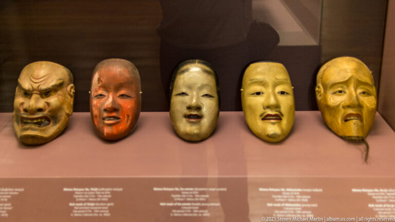 Five Japanese theatrical masks displayed in a row, with expressions ranging from fierce and grimacing to calm and aged.