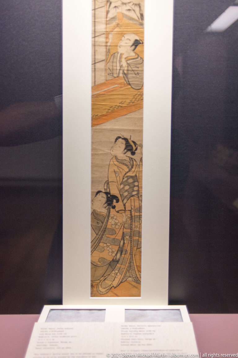 Vertical Japanese hanging scroll with two seated figures in separate painted scenes, mounted on a broad pale surround.