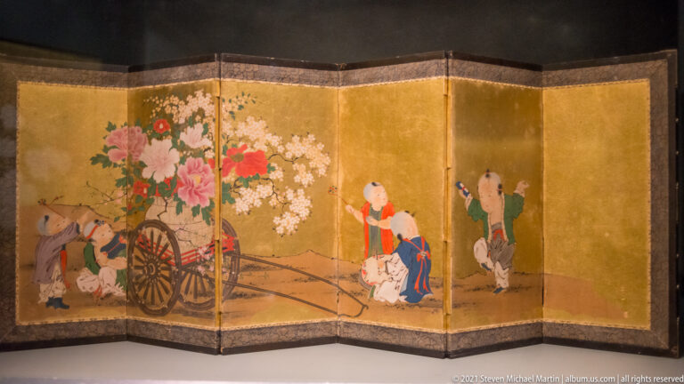 Gold-ground folding screen with several figures around a cart overflowing with pink, red, and white flowers.