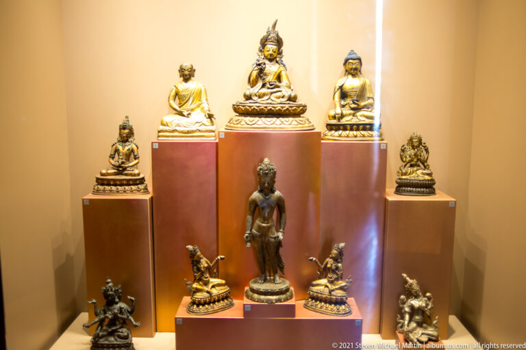 Bronze Buddhist figures on stepped plinths, with seated images behind a central standing figure and smaller figures below.