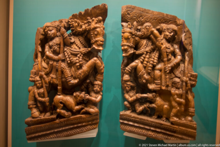 Pair of carved wooden relief panels with richly adorned standing figures, smaller attendants, animals, and decorative borders.