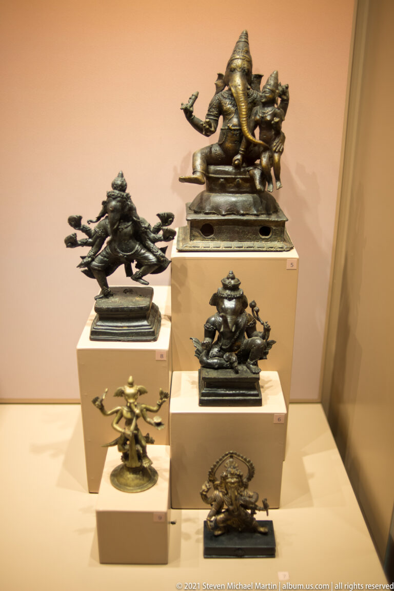 Tiered display of small Hindu metal sculptures, including a prominent seated elephant-headed Ganesha and other deities.