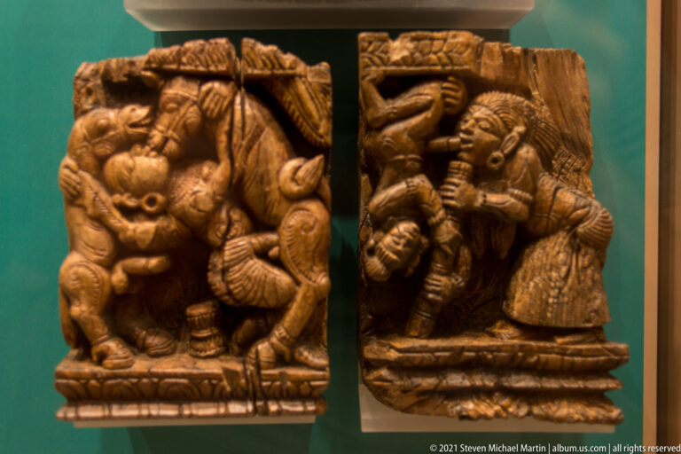 Two small wooden high-relief panels with robust deity figures, elaborate headdresses, jewelry, and deeply carved surrounding forms.