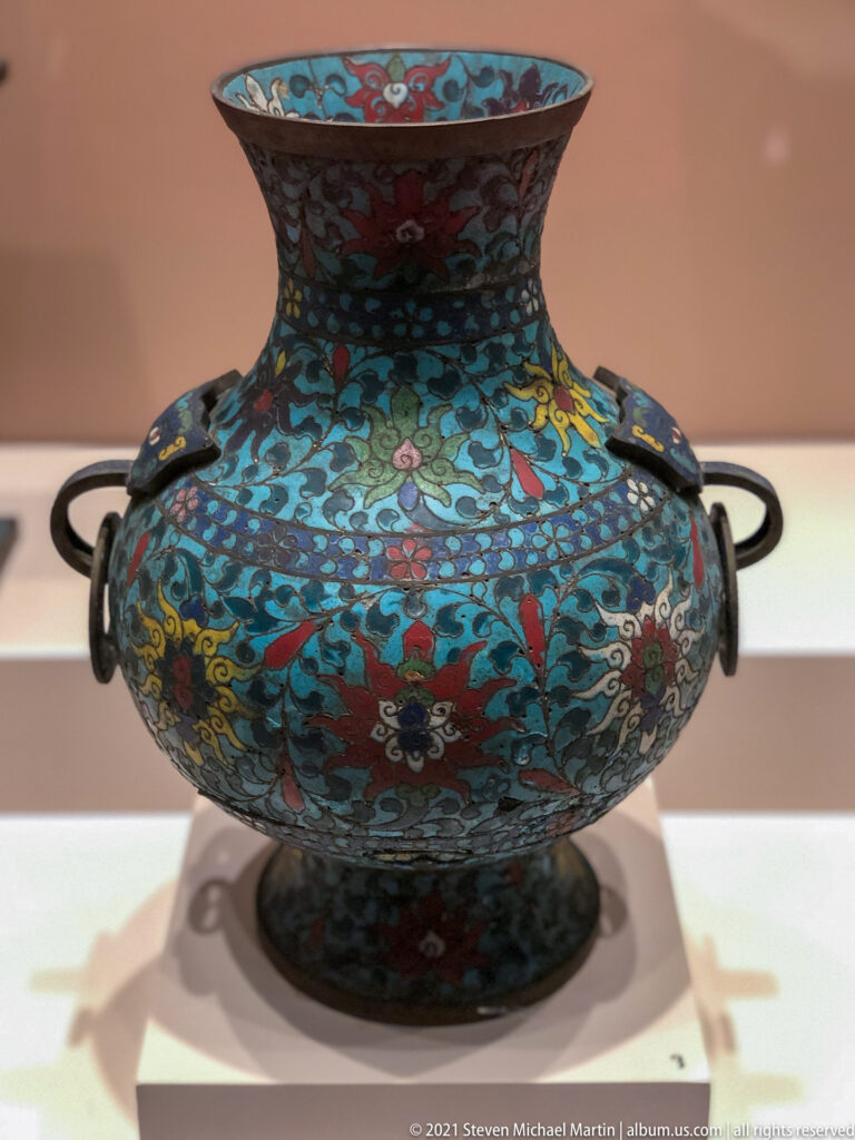 Turquoise cloisonné vase with flaring neck, rounded body, dark side handles, and dense multicolored floral scrolls.