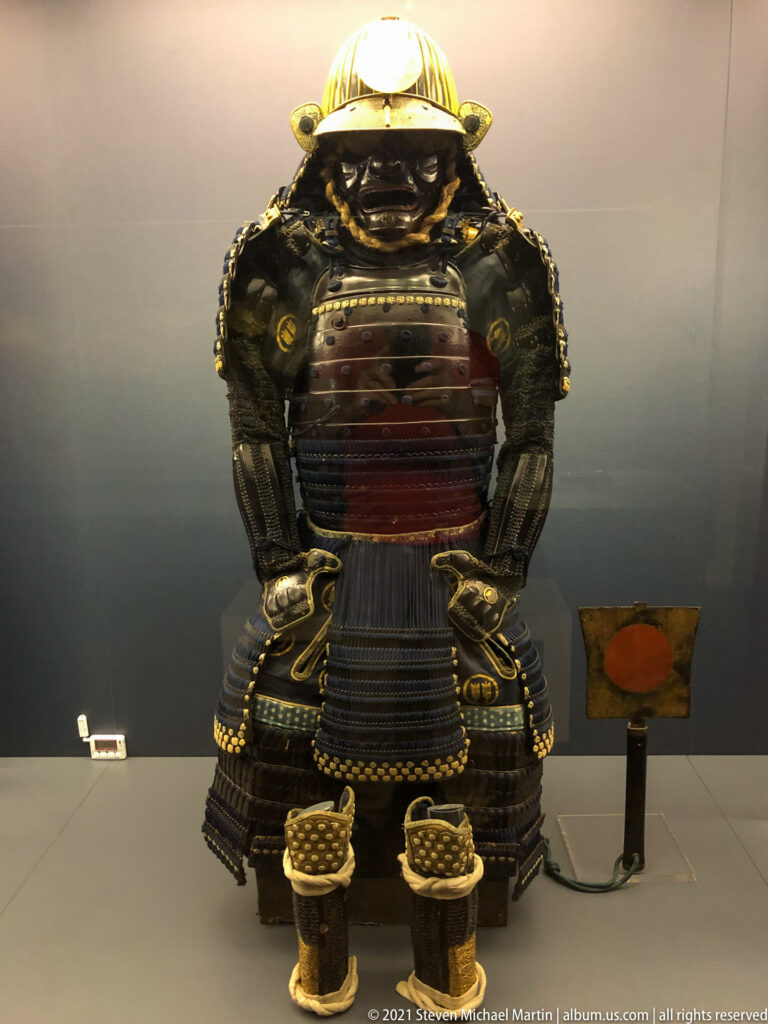 Complete Japanese samurai armor with helmet, face guard, layered cuirass and skirt defenses, plus separate armored footwear.