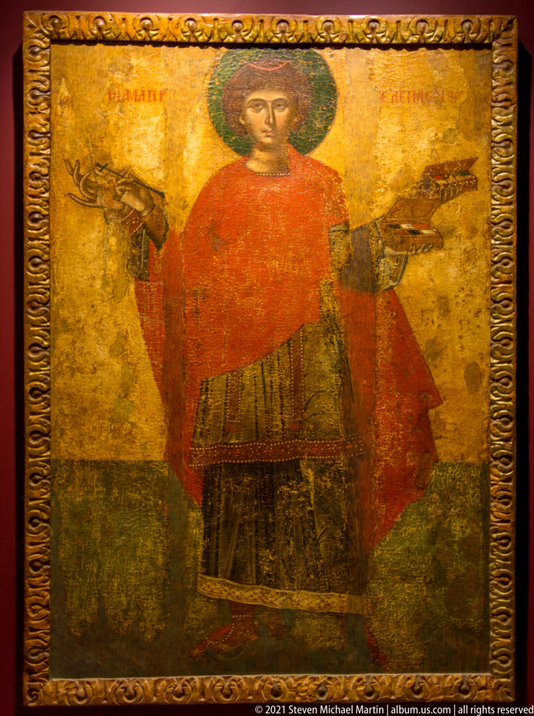 Full-length haloed saint in a red mantle on a worn gold-ground icon panel with decorative border.