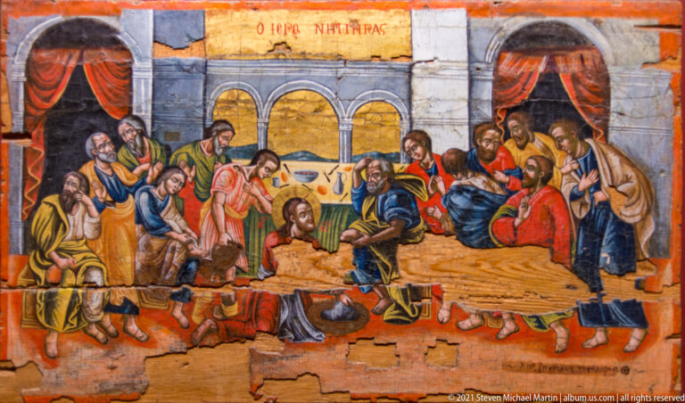Icon of Christ washing an apostle’s feet while the other apostles sit and stand in groups inside an architectural setting.
