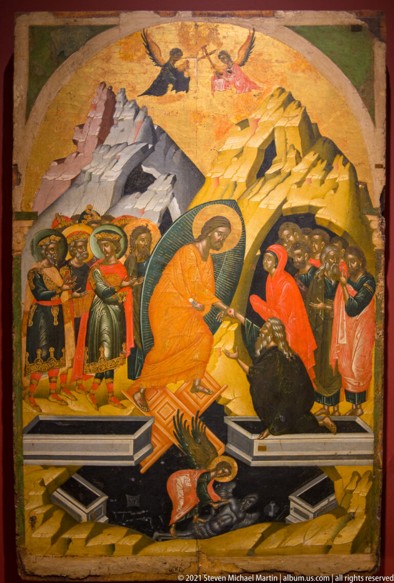 Anastasis icon with Christ in a mandorla raising a figure from a tomb as groups gather above broken doors and dark forms.