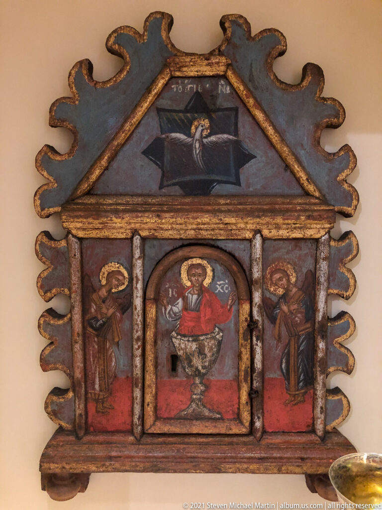 Small shrine-shaped triptych with Christ in the center, standing saints at the sides, and another sacred image in the triangular pediment.