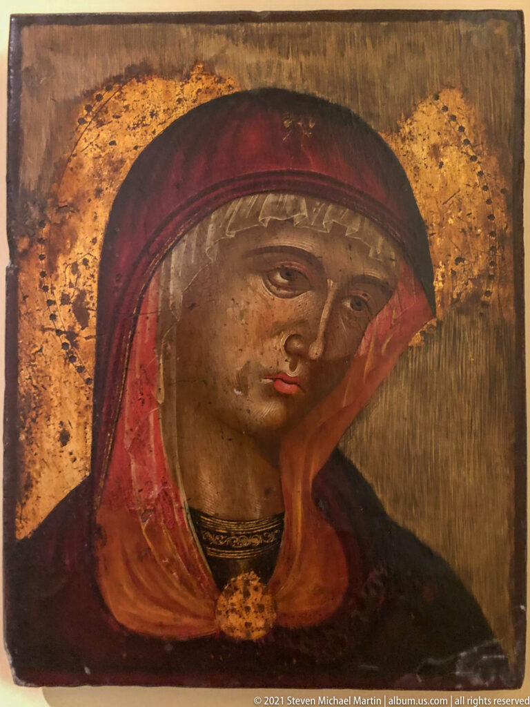 Bust-length icon of the Virgin Mary in a red head covering with gold halo on a worn gilded ground.