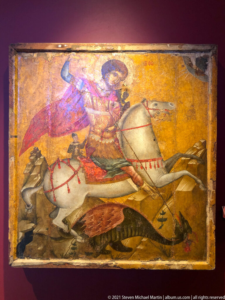 Saint George rides a white horse and thrusts a red spear into a dragon beneath him on a gold-ground icon.