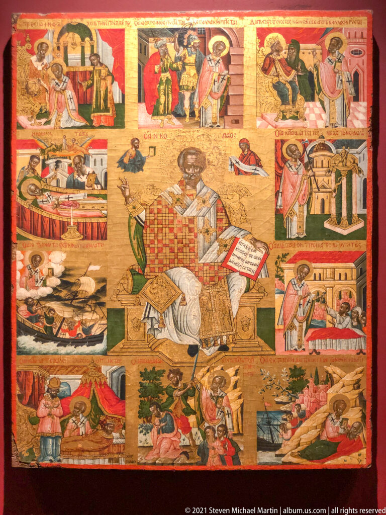 Narrative icon with a central seated monastic saint surrounded by many smaller inscribed scenes from a sacred life.