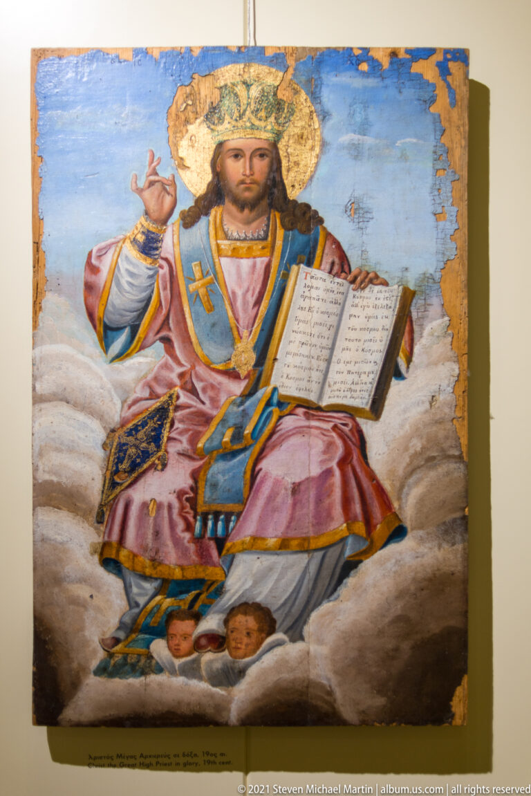 Icon of crowned Christ enthroned on clouds, blessing and holding an open inscribed Gospel, with angelic heads below.