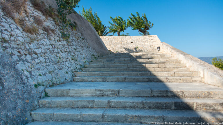 Broad stone staircase rising between masonry walls to the top of Heraklion's Venetian fortifications under strong sunlight.